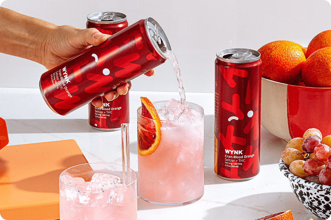 Glass of Cran-Blood Orange THC Seltzer with ice and a blood orange slice garnish, set against a vibrant red background for a refreshing, seasonal cannabis beverage.