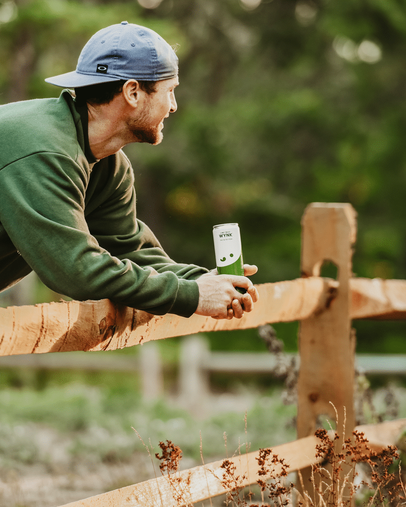 Man drinking Lime Twist Wynk, leaning on a fence.