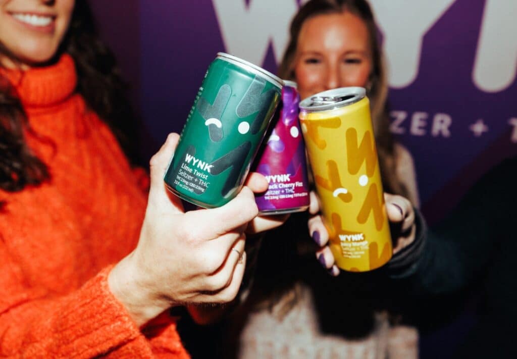 Chicago Nightlife wynk thc seltzer in chicago: Friends in Chicago cheerfully toast with WYNK THC and CBD beverages during Dry January, showcasing a selection of THC drinks including Lime Twist and Juicy Mango flavors. The image captures the festive and carefree spirit embraced by health-conscious consumers.