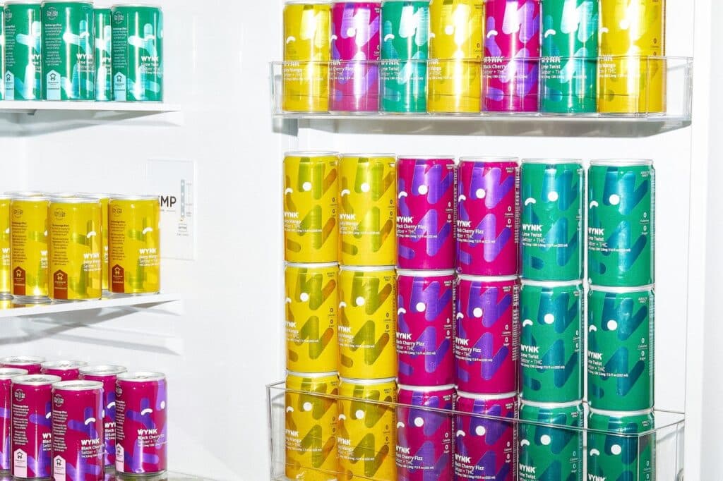 Assorted WYNK beverage cans, perfect for a Super Bowl party, featuring Juicy Mango, Lime Twist, and Black Cherry Fizz on a store shelf.